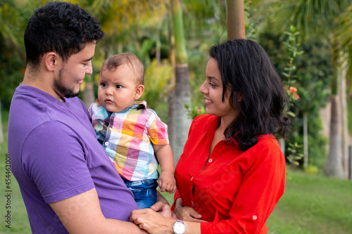 Happy parents taking care of their baby in a beautiful park full of nature. latin family concept.