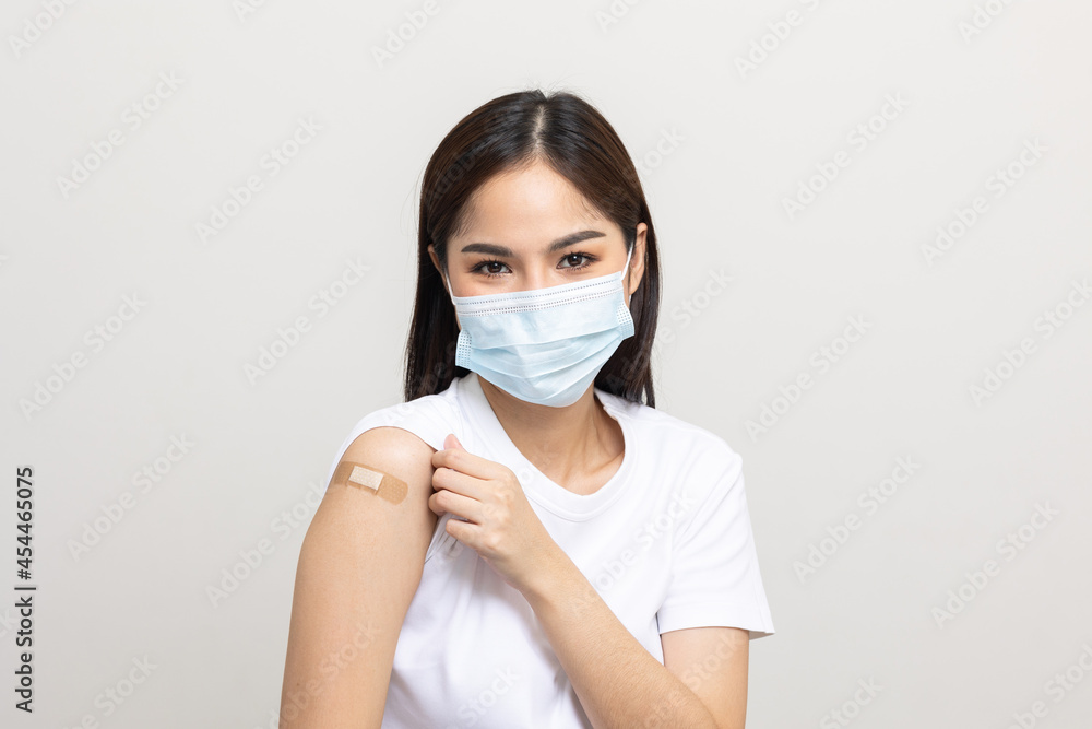 Young beautiful asian woman wearing mask and getting a vaccine protection the coronavirus. Happy female showing arm with bandage after receiving vaccination on isolated white background. Young beautiful asian woman wearing mask and getting a vaccine protection the coronavirus. Happy female showing arm with bandage after receiving vaccination on isolated white background.