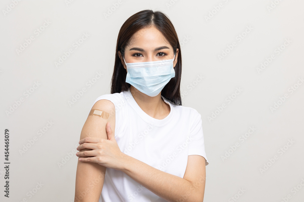 Young beautiful asian woman wearing mask and getting a vaccine protection the coronavirus. Happy female showing arm with bandage after receiving vaccination on isolated white background. Young beautiful asian woman wearing mask and getting a vaccine protection the coronavirus. Happy female showing arm with bandage after receiving vaccination on isolated white background.