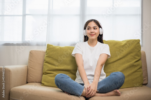 Relaxing time on sofa. Beautiful young asian woman sitting on sofa she choose music from smartphone take a rest and listening song with headphone. Lifestyle in living room at house in the morning.