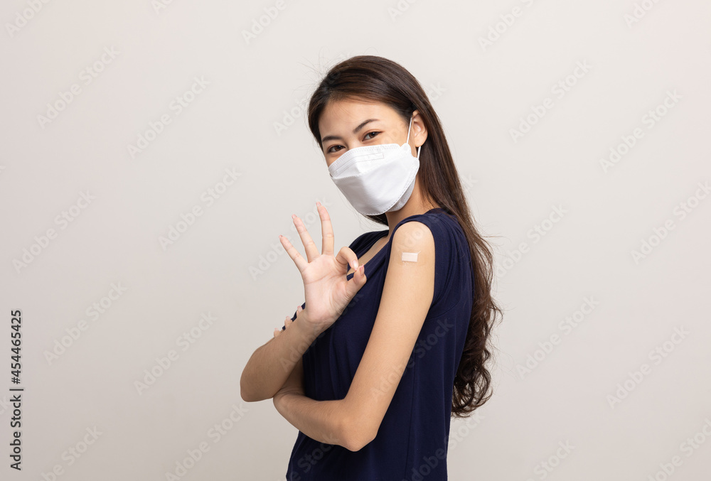 Young beautiful asian woman wearing mask and getting a vaccine protection the coronavirus. Happy female showing arm with bandage after receiving vaccination on isolated white background. Young beautiful asian woman wearing mask and getting a vaccine protection the coronavirus. Happy female showing arm with bandage after receiving vaccination on isolated white background.