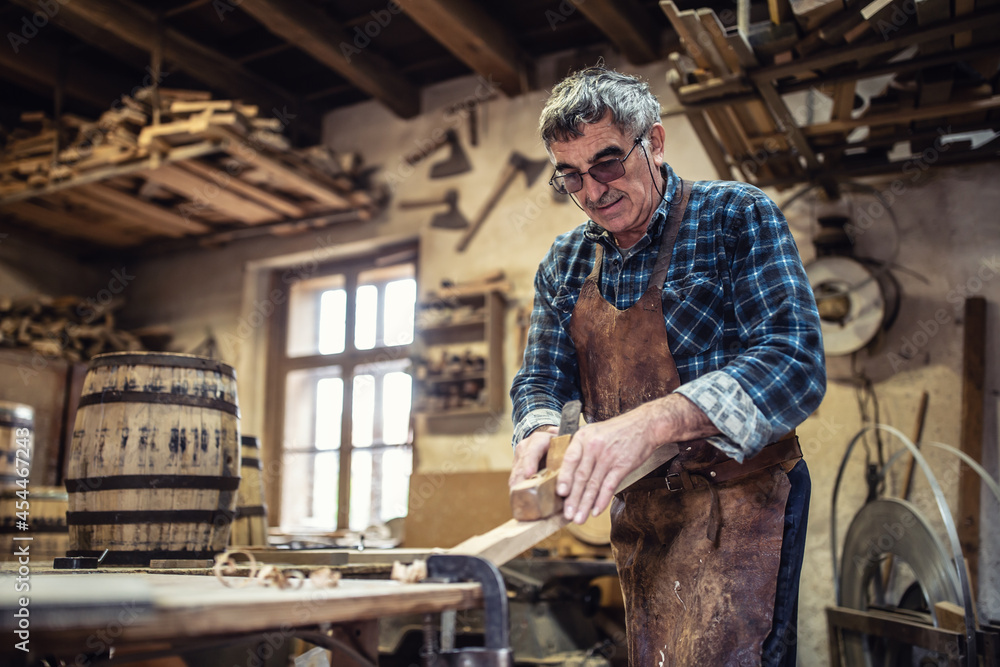 Carpenter in glasses uses jack-plane to smooth the surface of wood in the workshop