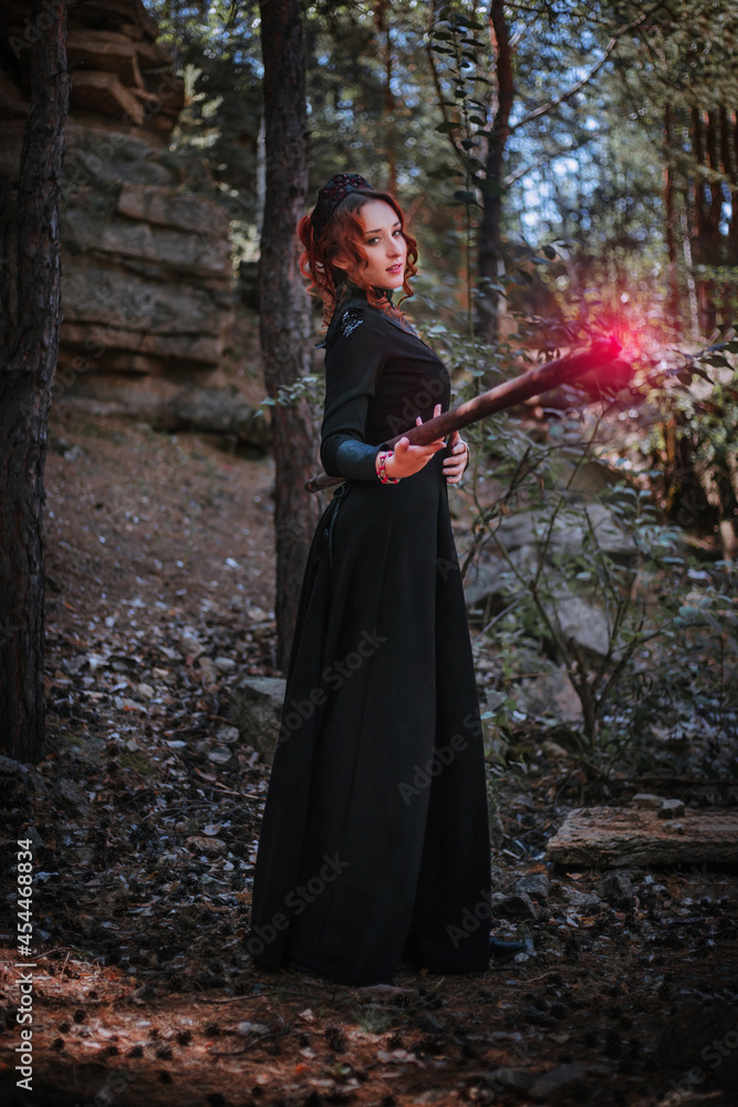 A witch in a black long dress of the Slavic style holds a staff in her hands.