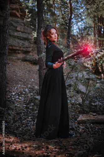 A witch in a black long dress of the Slavic style holds a staff in her hands.