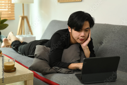 Casual man lying on couch and using computer tablet.
