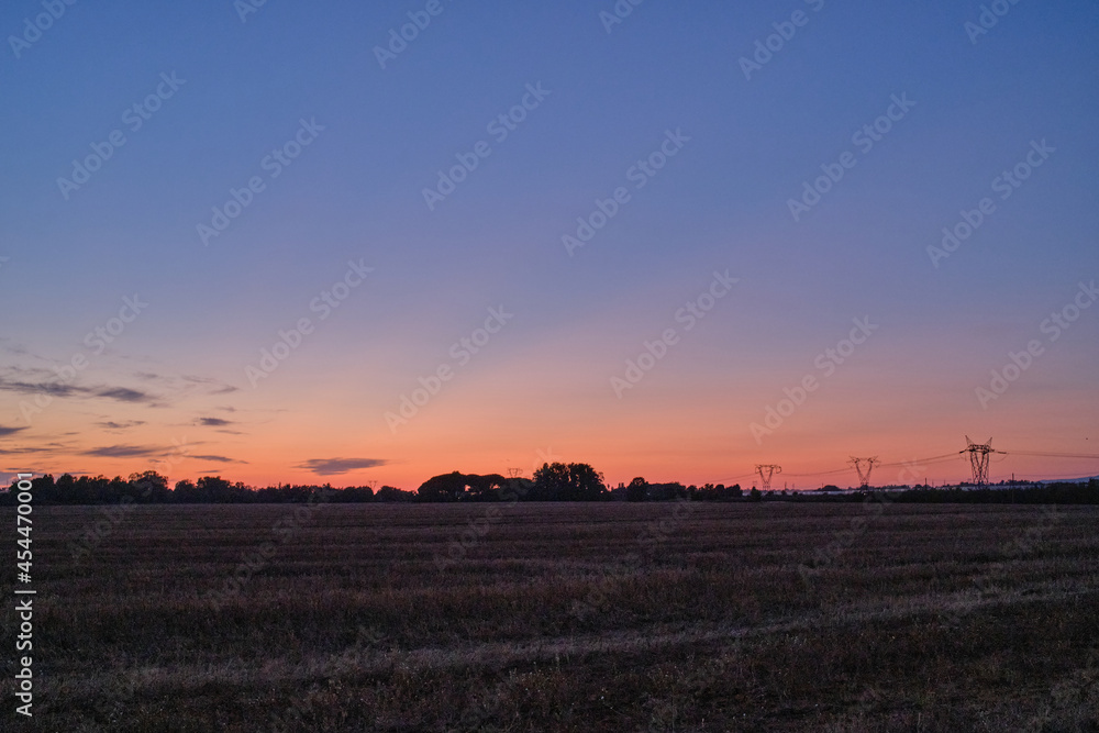 Sunset over a cultivated field in latium and power lines in the background