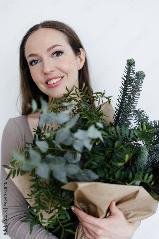 portrait of a Caucasian young woman florist with a winter bouquet in her hands. a bouquet of greenery in tap paper. Christmas and New Year. portrait of a Caucasian young woman florist with a winter bouquet in her hands. a bouquet of greenery in tap paper. Christmas and New Year.