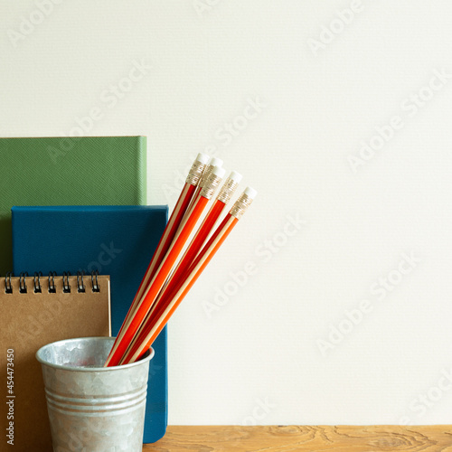 Notebooks, orange pencils on wooden desk. ivory wall background