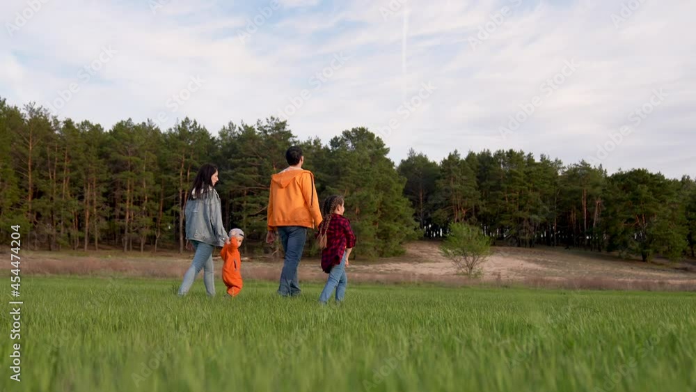Happy family is walking on green grass. Mom dad and girl with toddler in park at sunset. Happy family walking in park at sunset. Mom dad girl and baby on green grass. Happy family concept at sunset Happy family is walking on green grass. Mom dad and girl with toddler in park at sunset. Happy family walking in park at sunset. Mom dad girl and baby on green grass. Happy family concept at sunset