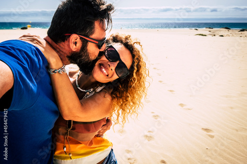 Happy adult couple kissing and taking selfie picture during summer fun holiday vacation together - ebach and ocean in background - people outdoor love leisure activity photo