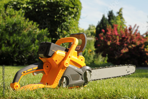 New yellow chainsaw for wood in the grass in garden - side view