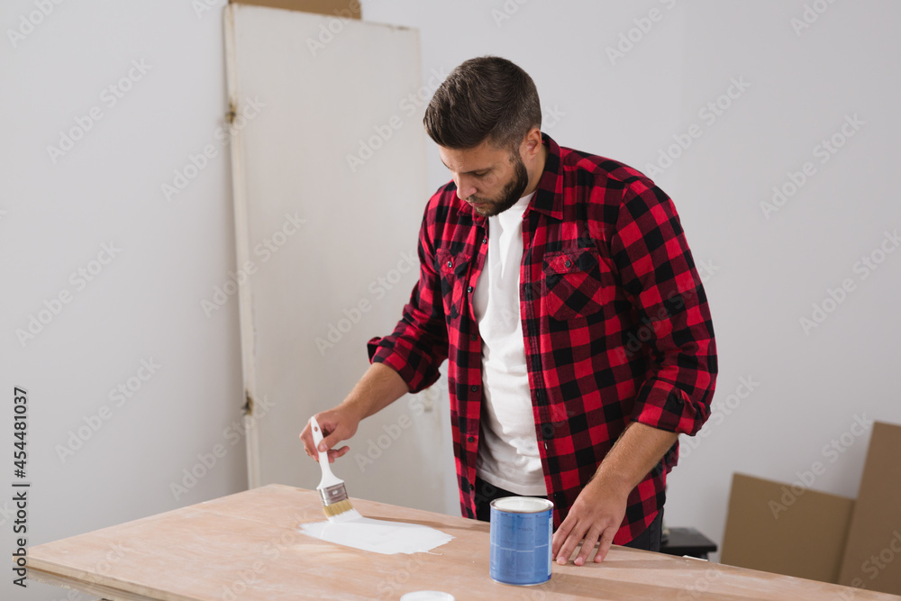 man repairing old door. he is painting with white paint
