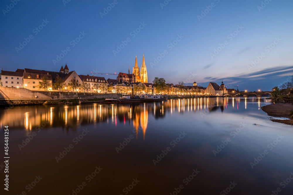 Regensburg während der blauen Stunde im Zwielicht mit Donau beleuchteter Promenade Dom und steinerne Brücke, Deutschland