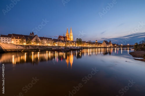 Regensburg während der blauen Stunde im Zwielicht mit Donau beleuchteter Promenade Dom und steinerne Brücke, Deutschland