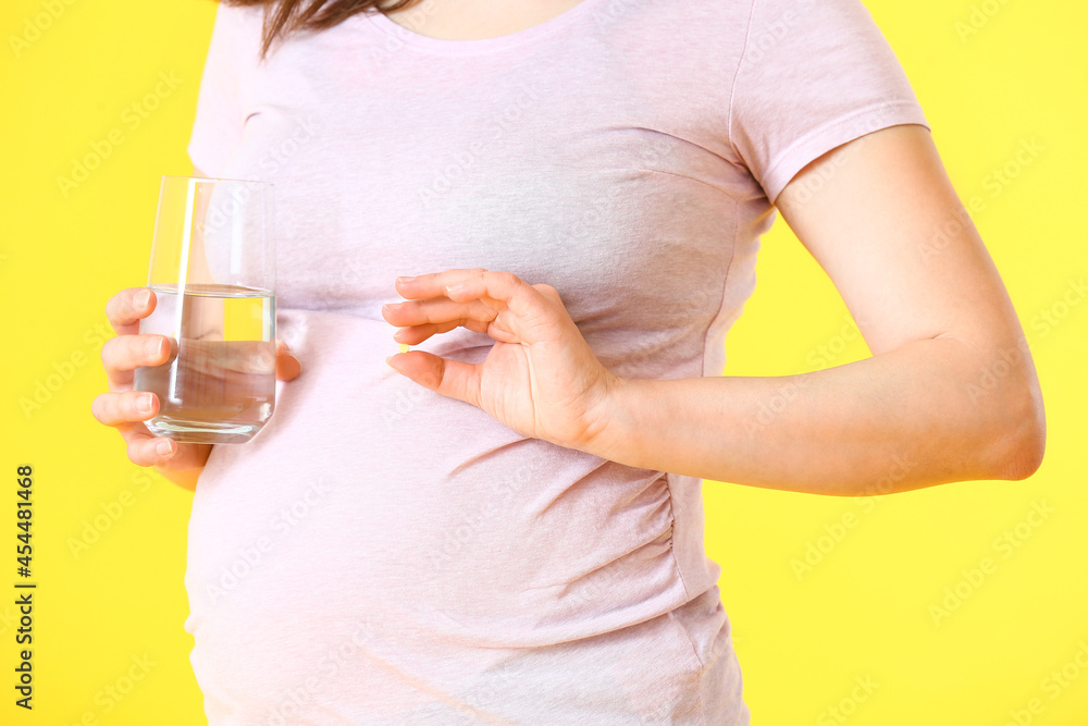 Young pregnant woman with pills and glass of water on color background Young pregnant woman with pills and glass of water on color background