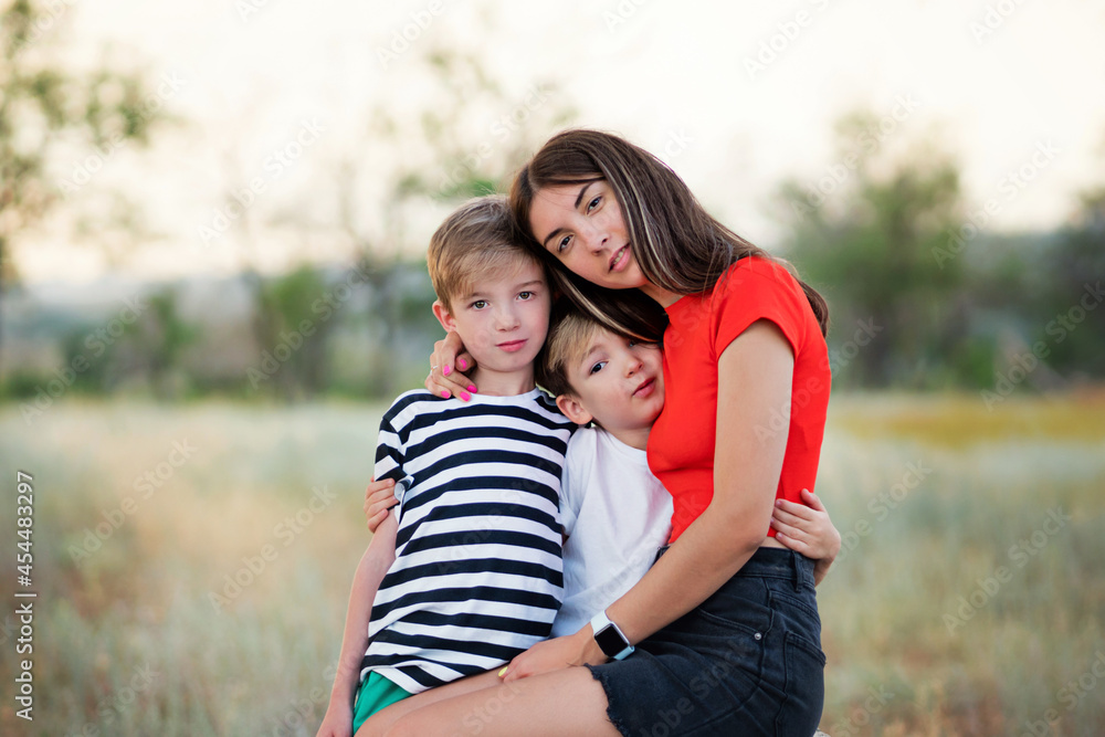 Fototapeta premium Candid authentic family portrait. Casual mom with two sons in confidential conversation In Rural Settings. Young woman with children on countryside background