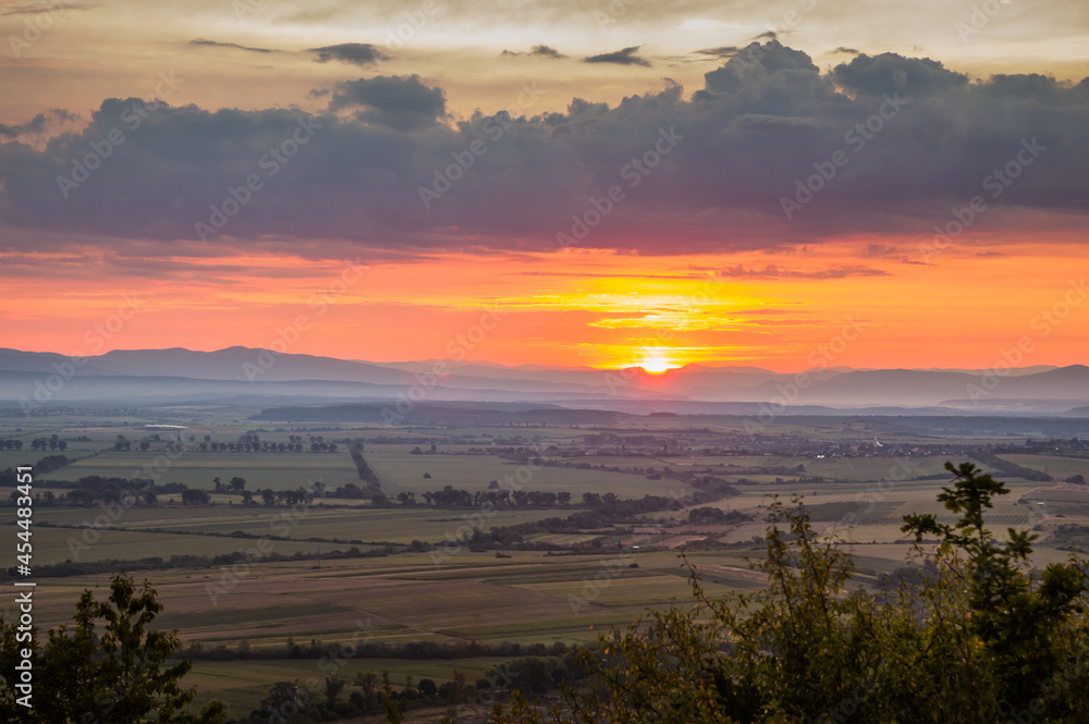 Obraz premium Dawn in the mountains. The sun rises from behind the mountains. Beautiful green hills and green valley. Little sleeping town. A colorful sky, red clouds. Mountains in the fog. Carpathian, Ukraine,