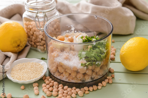 Blender with chickpeas and ingredients for hummus on color wooden background
