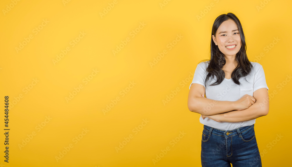 Portrait of smiling Asian woman with long dark hair wears white t-shirt crossed arms isolated on yellow background, copy space Portrait of smiling Asian woman with long dark hair wears white t-shirt crossed arms isolated on yellow background, copy space