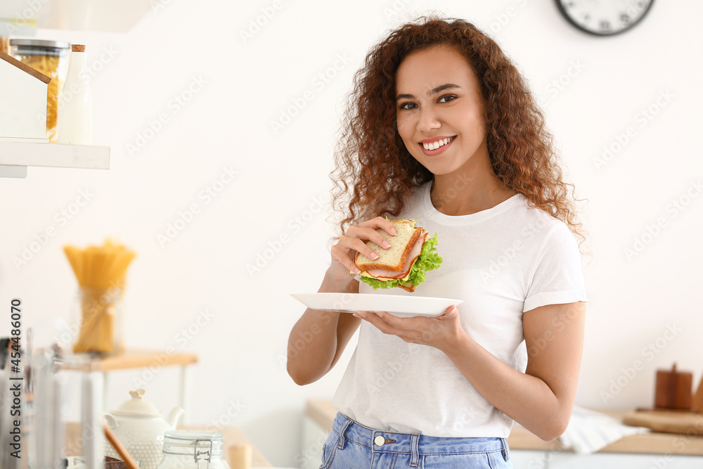 Young African-American woman with tasty sandwich in kitchen Young African-American woman with tasty sandwich in kitchen