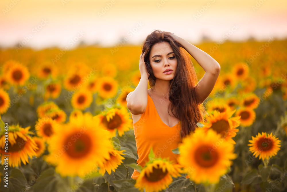 Beautiful young girl enjoying nature on the field of sunflowers at sunset. Summertime. Attractive brunette woman with long healthy hair. Beautiful young girl enjoying nature on the field of sunflowers at sunset. Summertime. Attractive brunette woman with long healthy hair.
