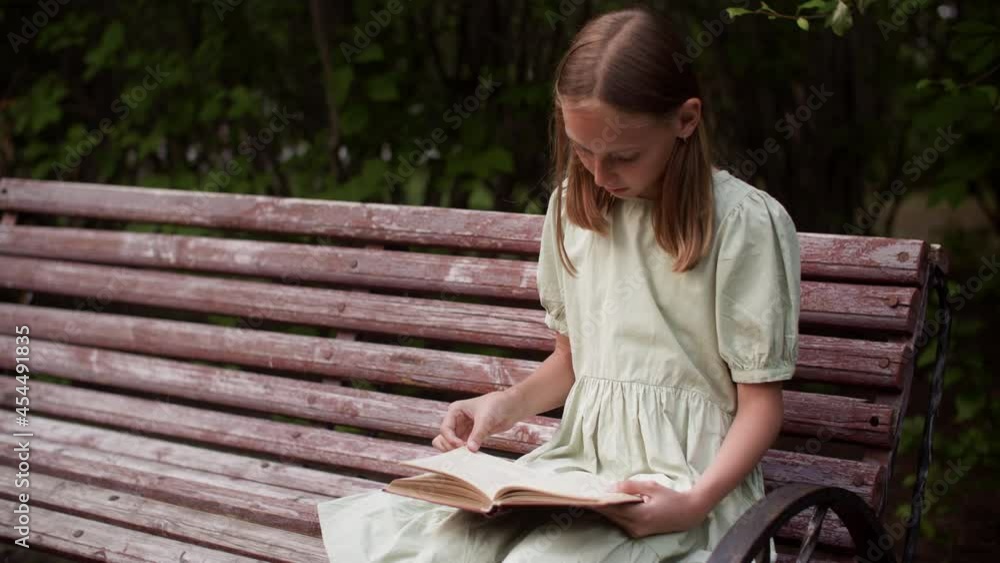 Teenager girl leafing through book sitting on park bench at summer weekend. Serious teen girl reading book on bench in summer garden Teenager girl leafing through book sitting on park bench at summer weekend. Serious teen girl reading book on bench in summer garden