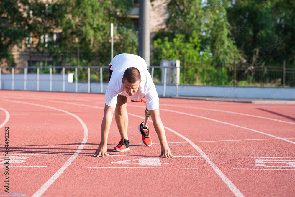 Caucasian male athlete with a prosthetic leg standing at the start on the track at the stadium. Sport concept.