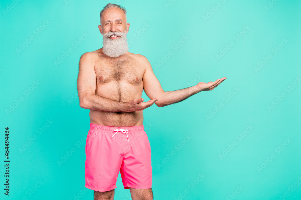 Photo of reliable cheerful mature man hands presenting empty space wear pink shorts isolated turquoise color background
