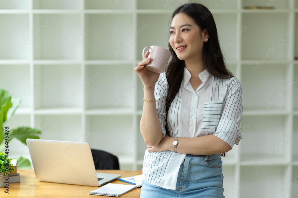 Successful young female entrepreneur relax standing with coffee cup in modern workplace Successful young female entrepreneur relax standing with coffee cup in modern workplace