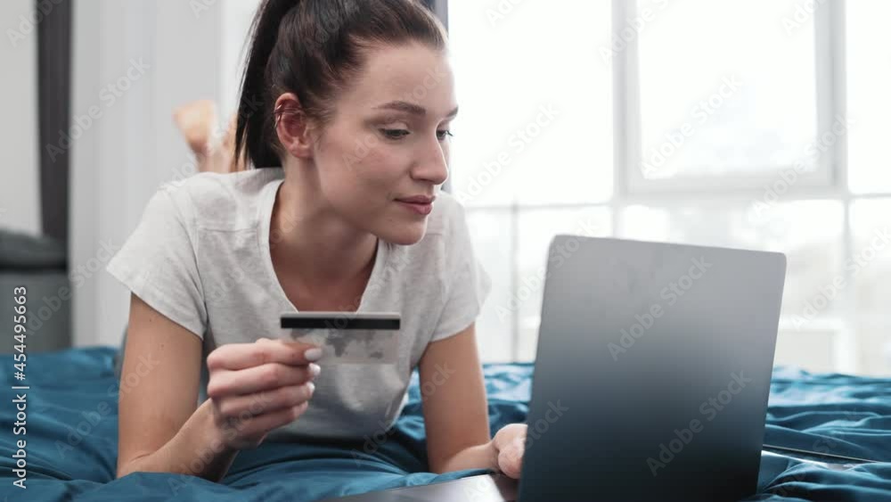 A happy woman using laptop while transferring money lying on the bed at home A happy woman using laptop while transferring money lying on the bed at home