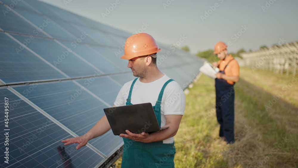 Engineer standing with Solar cell panels looking monitor of the Electric power value made from the solar cell. Man holding laptop in her hands standing on field with solar panels. Engineer standing with Solar cell panels looking monitor of the Electric power value made from the solar cell. Man holding laptop in her hands standing on field with solar panels.