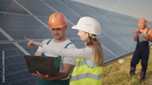 Technician and investor walking in Solar cell Farm through field of solar panels checking the panels at solar energy installation. Employees of power plant and talking about scheme of solar panels.