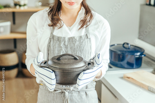 キッチンで女性がミトンをつけて両手で鍋を持っている　woman kitchen photo