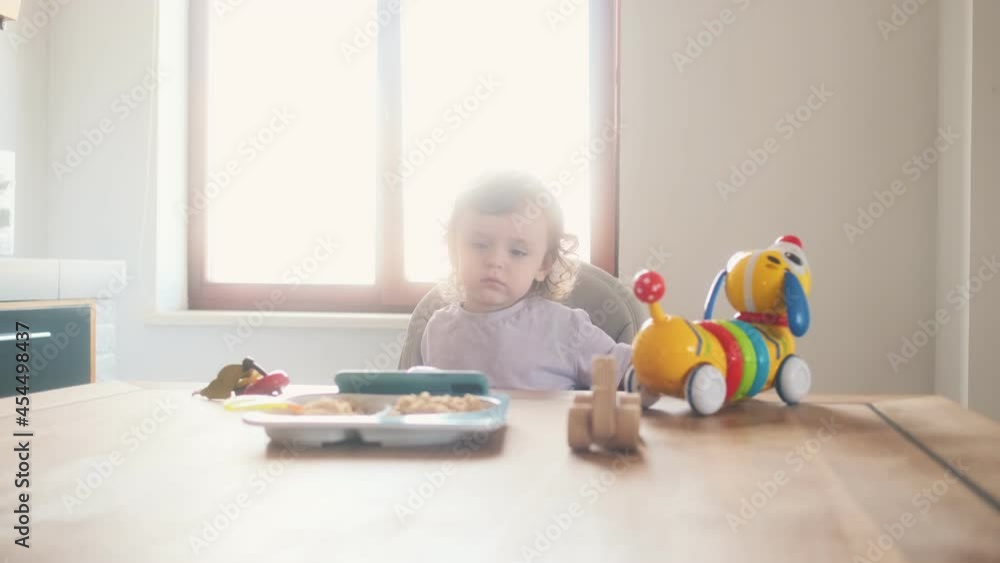 A lovely baby sitting in the child chair and watching mobile in the kitchen at home A lovely baby sitting in the child chair and watching mobile in the kitchen at home