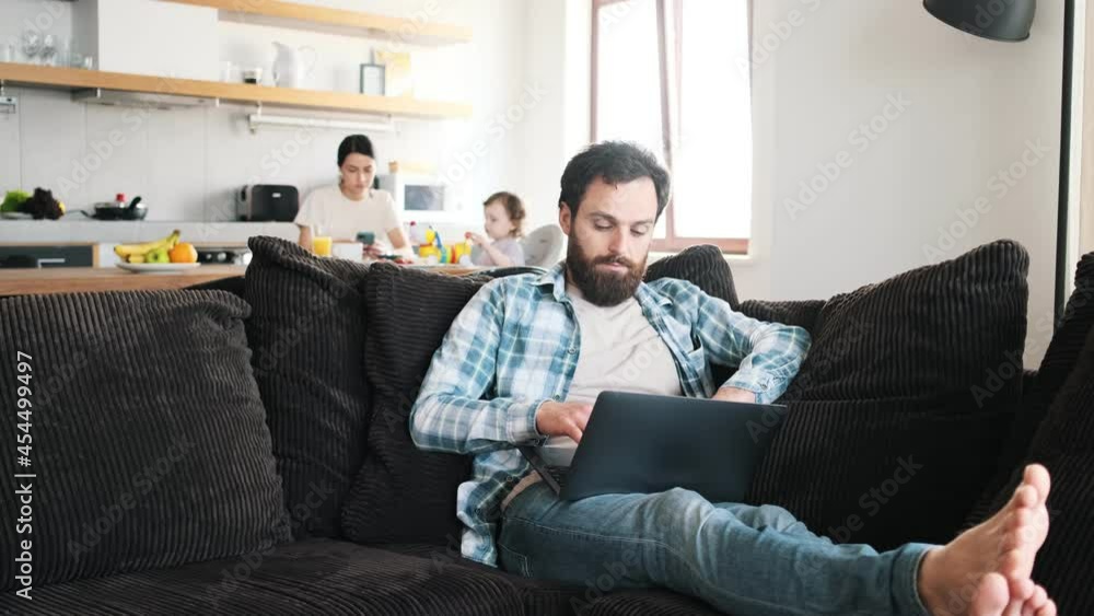 A focused father using his laptop while sitting on the sofa in the living room at home A focused father using his laptop while sitting on the sofa in the living room at home