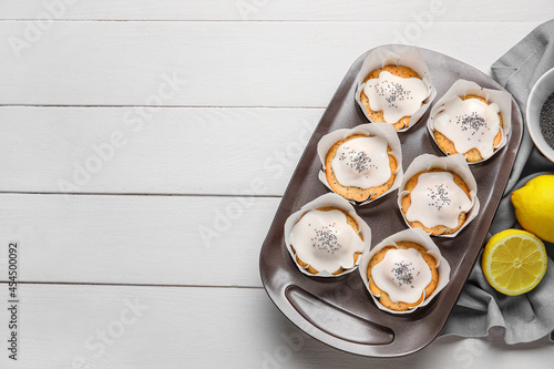 Baking tin with delicious glazed poppy seed muffins on white wooden background