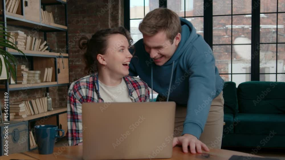 Pan left view of happy young man and woman looking at screen and laughing while browsing netbook at home together Pan left view of happy young man and woman looking at screen and laughing while browsing netbook at home together