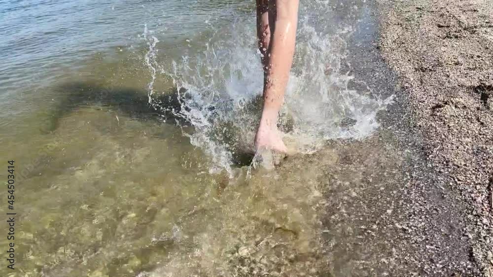 Back view of legs. A young boy runs along the beach splashing water drops. Slow motion Back view of legs. A young boy runs along the beach splashing water drops. Slow motion