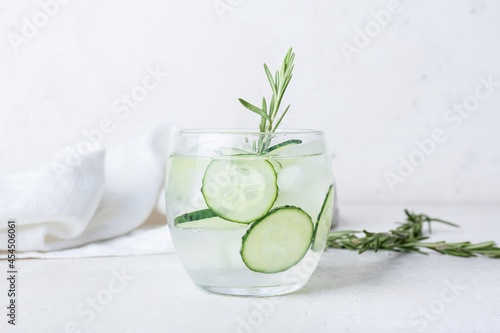 Glass of cold gin tonic and cucumber slices on light background