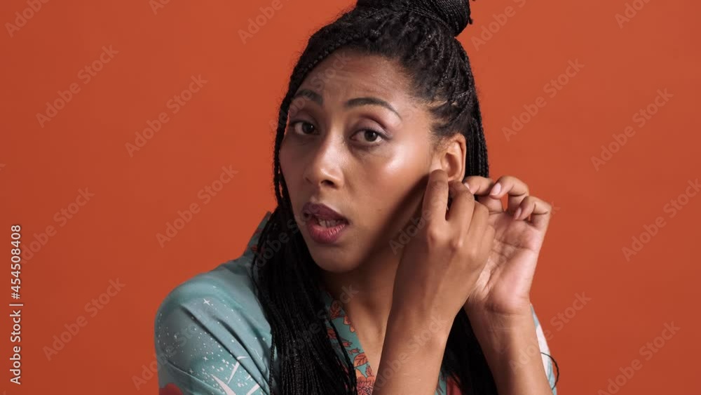 A close-up view of a fashionable african american woman looking to the mirror standing isolated over a red background in the studio A close-up view of a fashionable african american woman looking to the mirror standing isolated over a red background in the studio