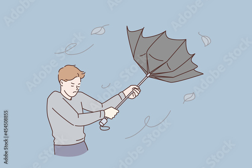 Bad weather and storm concept. Young stressed man cartoon character standing trying to catch flying umbrella from rain and wind vector illustration 