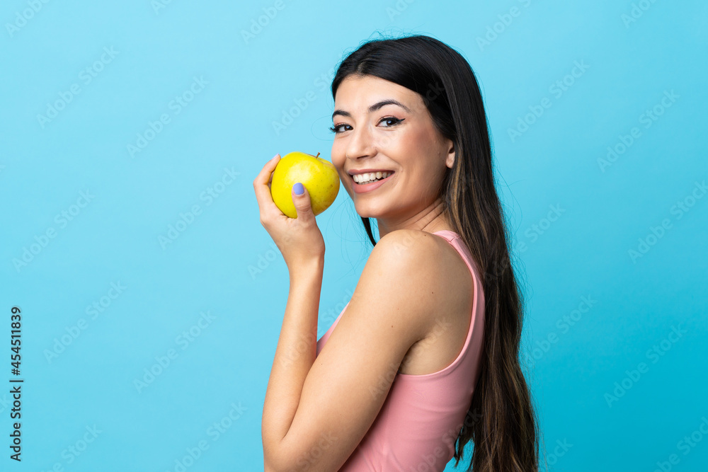 Young brunette girl over isolated blue background eating an apple Young brunette girl over isolated blue background eating an apple