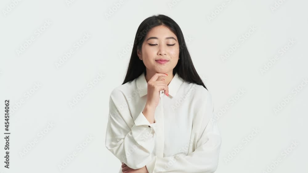 Pleased asian korean woman pondering while coming up with an idea standing isolated over white background in the studio Pleased asian korean woman pondering while coming up with an idea standing isolated over white background in the studio