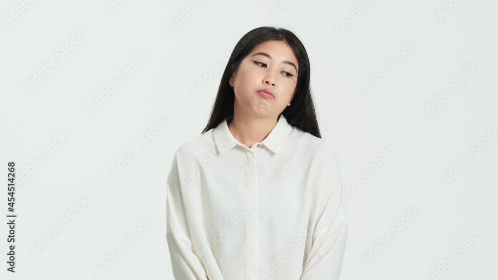 Bored displeased asian korean woman posing to the camera standing isolated over white background in the studio Bored displeased asian korean woman posing to the camera standing isolated over white background in the studio