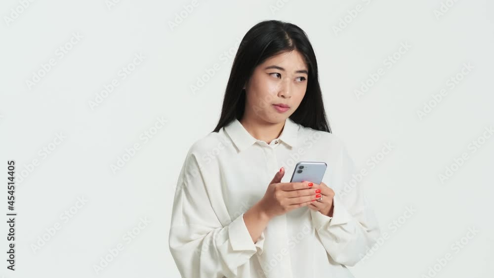 Beautiful asian korean woman using her phone standing isolated over white background in the studio Beautiful asian korean woman using her phone standing isolated over white background in the studio