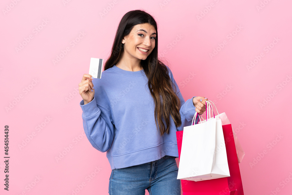 Young brunette girl over isolated pink background holding shopping bags and a credit card Young brunette girl over isolated pink background holding shopping bags and a credit card