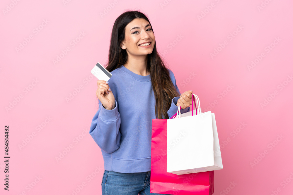 Young brunette girl over isolated pink background holding shopping bags and a credit card Young brunette girl over isolated pink background holding shopping bags and a credit card