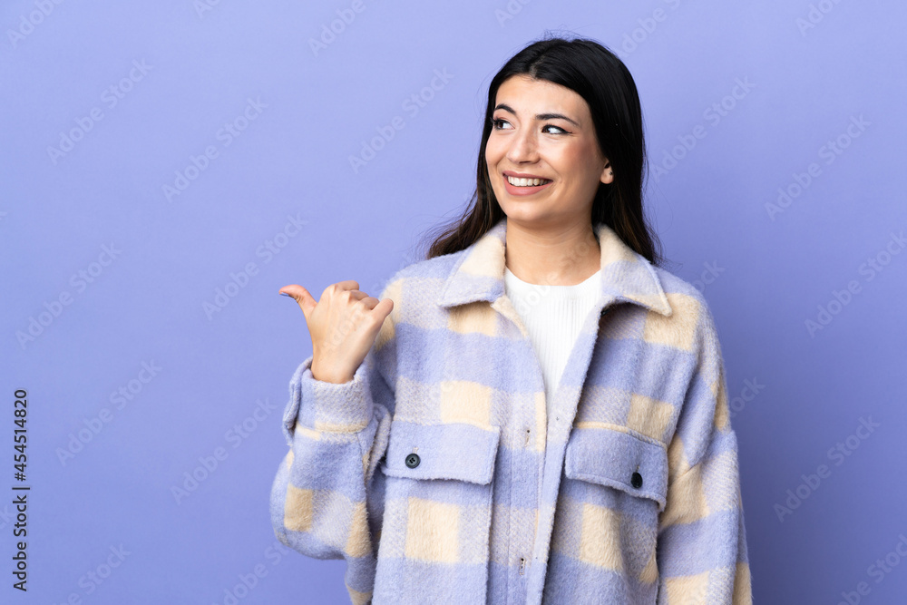 Young brunette woman over isolated purple background pointing to the side to present a product Young brunette woman over isolated purple background pointing to the side to present a product