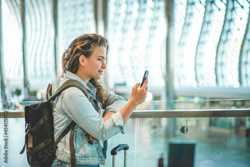 A beautiful caucasian young woman using mobile phone at airport to buy tickets online, book hotel, or rent a car. Covid time travels, space for text