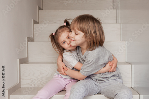 two young children brother and sister hugging at home on a wooden staircase. High quality photo